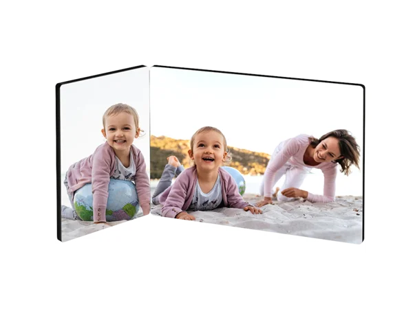 Ein zweiteiliger Fotoaufsteller zeigt eine fröhliche Szene am Strand. Auf der linken Seite sitzt ein kleines Mädchen auf einem bunten Ball und lächelt.