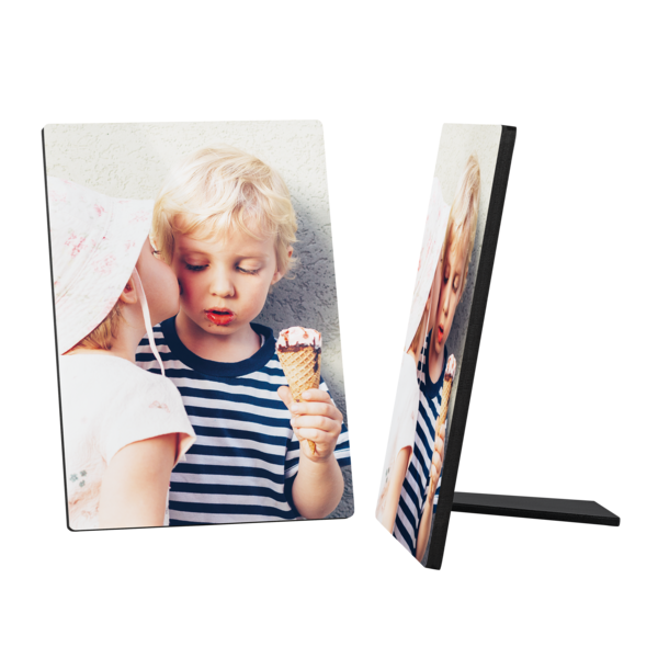 Ein Fotoaufsteller zeigt ein süßes Bild von zwei kleinen Kindern. Ein blondhaariger Junge mit einem blau-weiß gestreiften Shirt hält ein Eis in der Hand und schaut darauf. Ein anderes Kind mit einem hellen Sonnenhut beugt sich zu ihm und scheint ihm einen Kuss auf die Wange zu geben. Der Hintergrund ist hell und schlicht. Rechts daneben ist ein weiterer Fotoaufsteller mit dem gleichen Motiv zu sehen, der auf seiner Stütze steht.